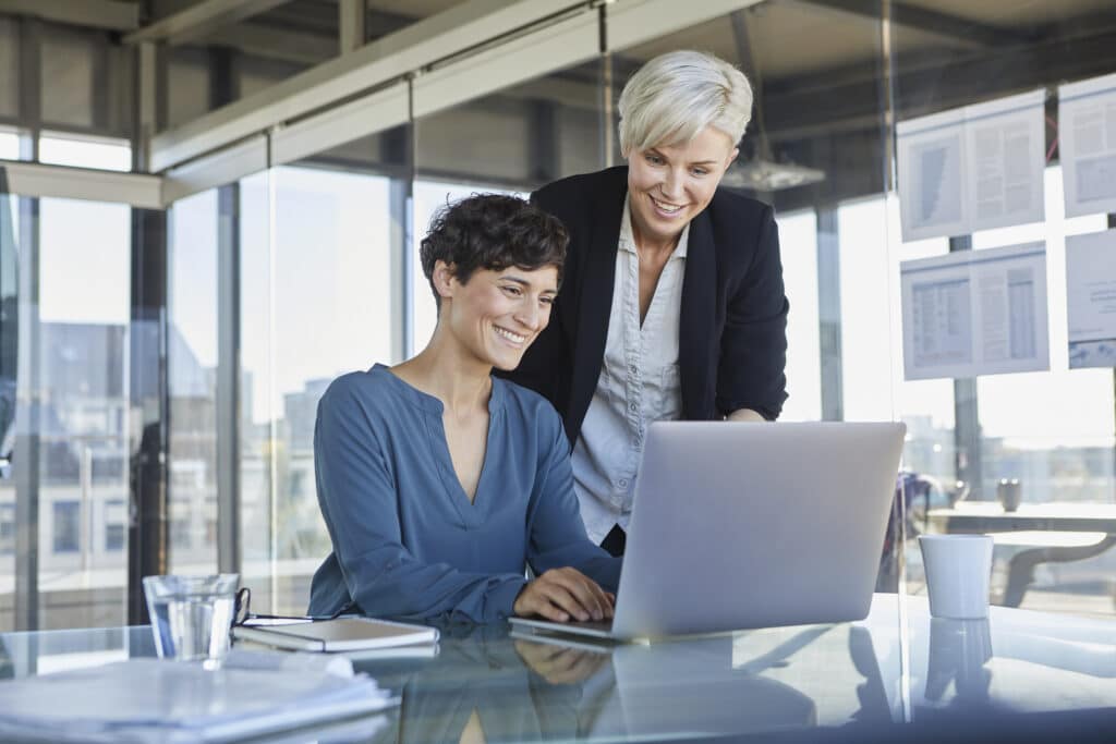 Coach pour entrepreneur : pourquoi et comment trouver le bon coach ? 2 two smiling businesswomen sharing laptop at desk i 2022 12 16 22 12 07 utc